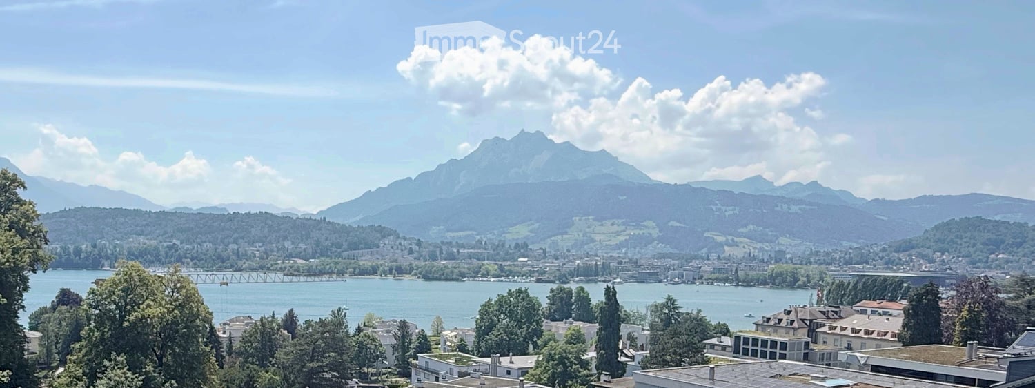 Panoramic view of a cityscape with a lake, mountains, and scattered buildings.