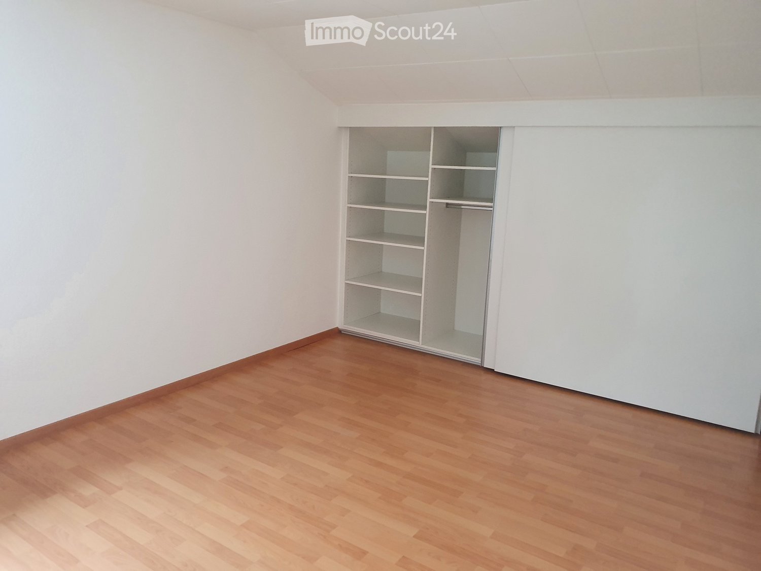 Empty room with wooden flooring and white walls, featuring an open closet with empty shelves and hanging space.