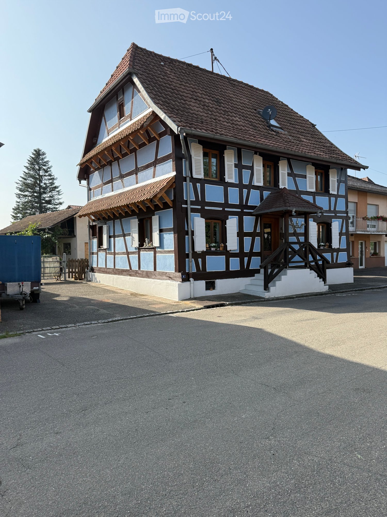 Traditional two-story house with a tiled roof, wooden beams, and white shutters. Features a small porch with steps and a satellite dish on the roof.