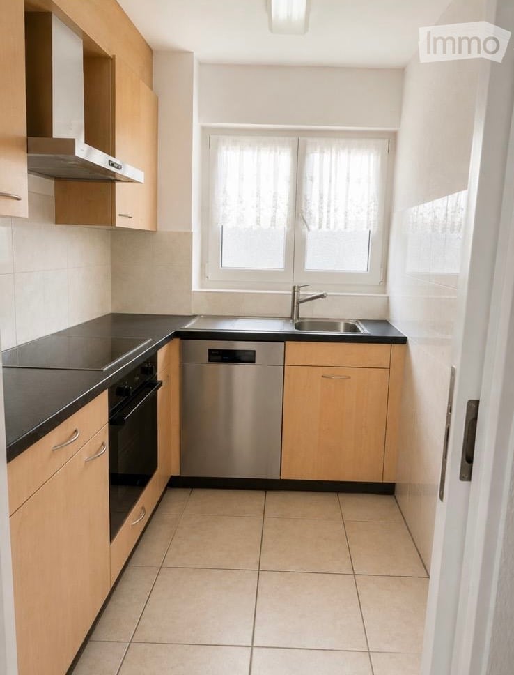 Modern kitchen with light wooden cabinets, black countertops, stainless steel sink and dishwasher, and tiled flooring.