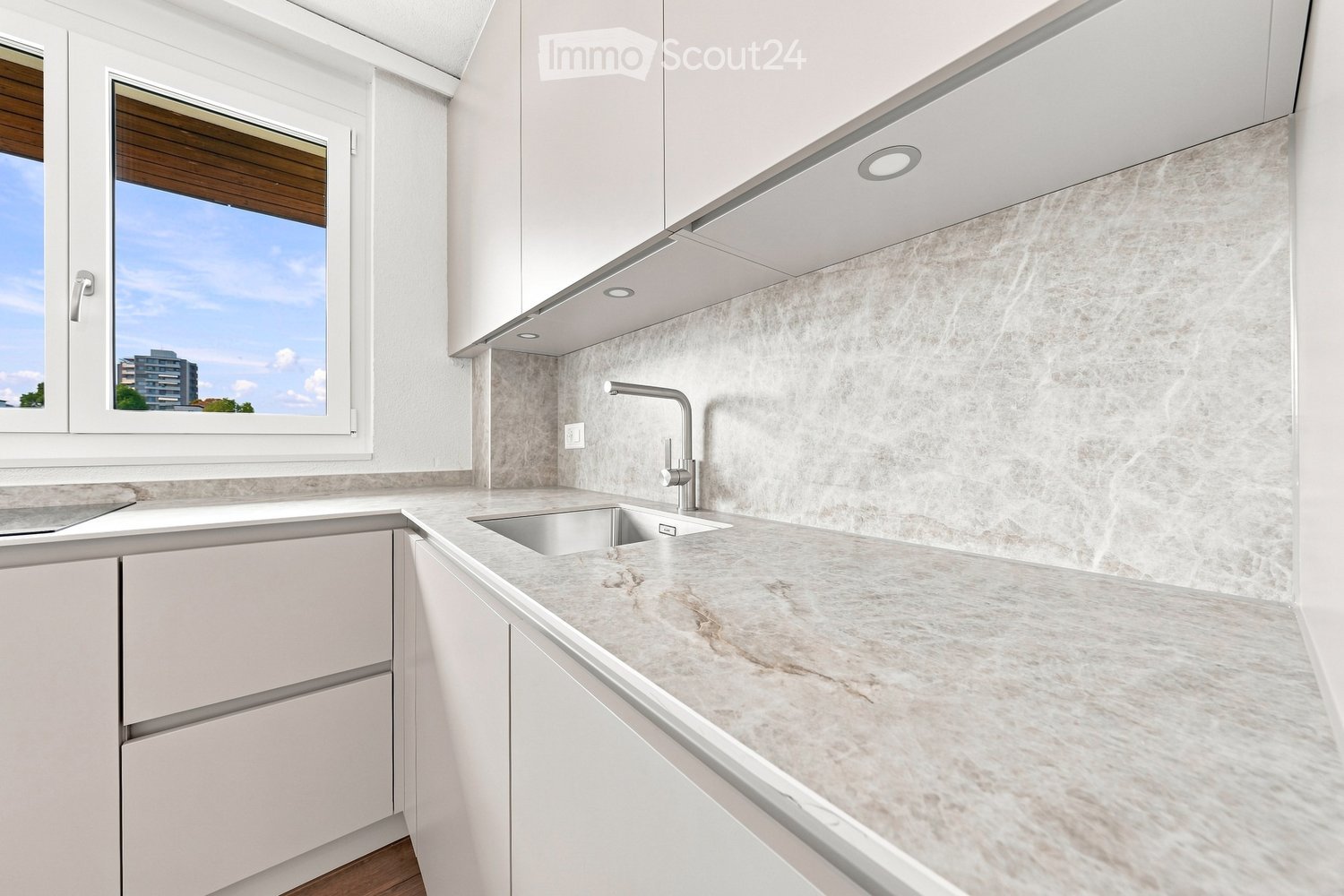 Modern kitchen with white cabinets, marble countertop, and a stainless steel sink with a modern faucet. The backsplash features a textured, light-colored tile design.