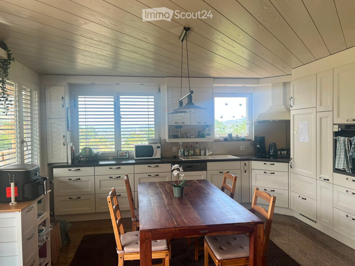 Bright kitchen with white cabinets, wooden dining table, four chairs, microwave, sink, oven, and various appliances.