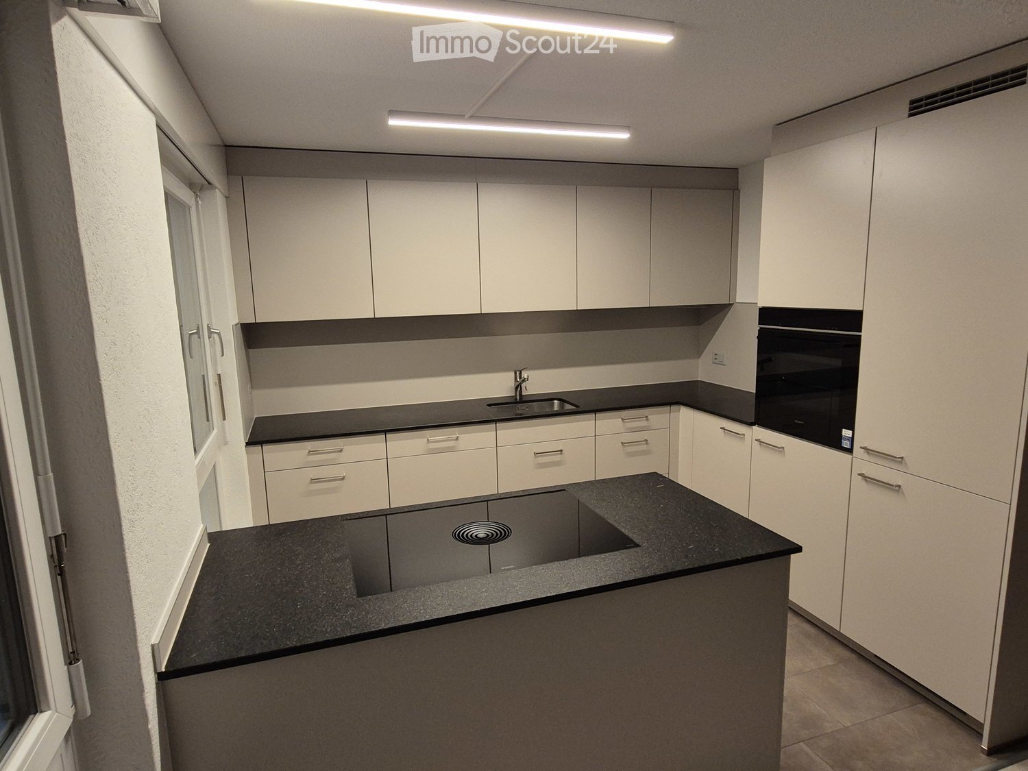 Modern kitchen with white cabinets, black countertops, and built-in appliances including a sink and oven.