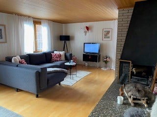 Bright living room with wooden ceiling and floors, grey sectional sofa, coffee table, TV, fireplace, and decorative items.