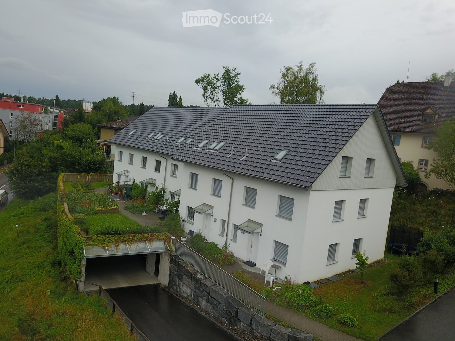 White house with gray roof, multiple windows, garden, garage, green roof, multiple plants