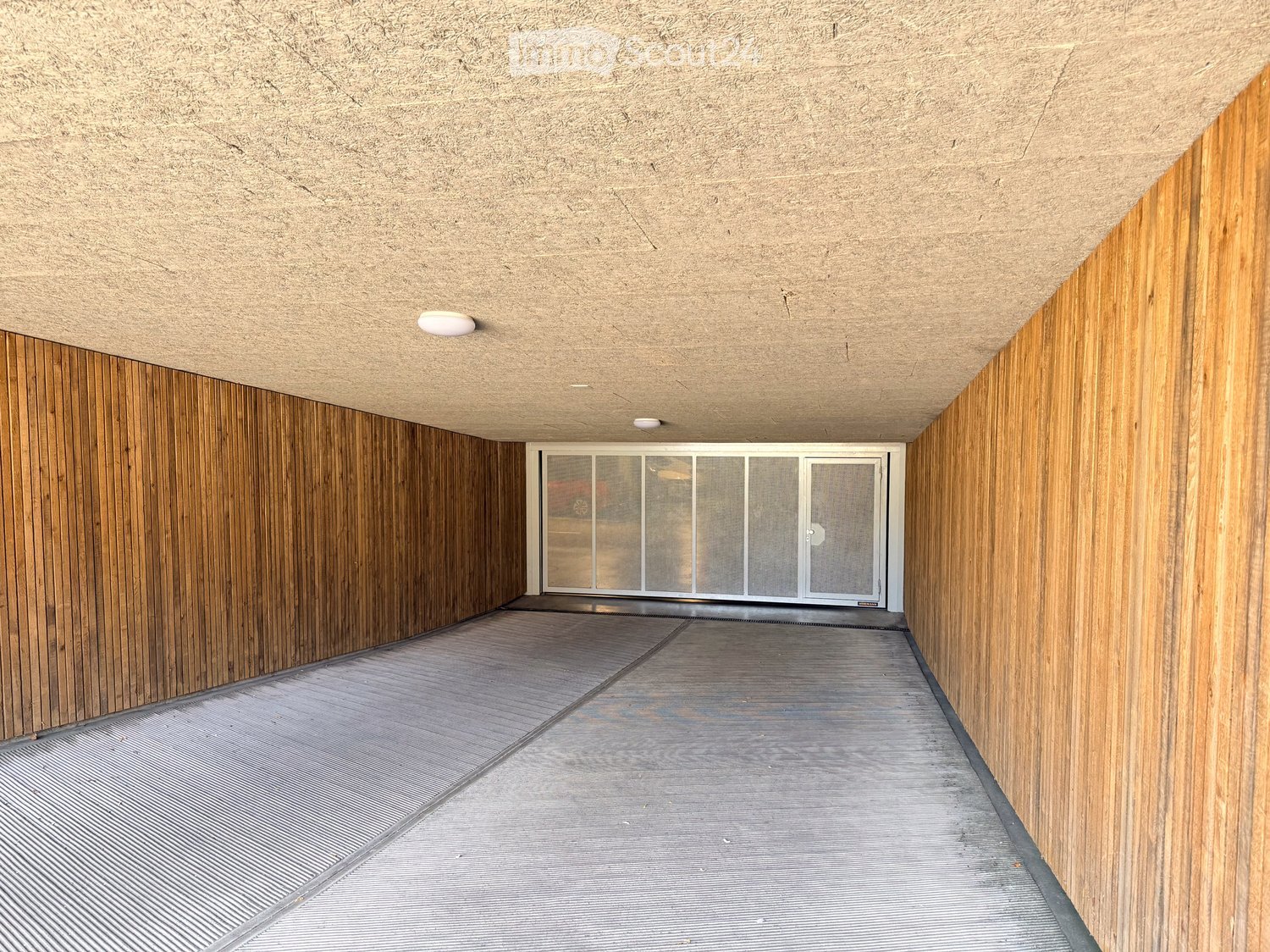 A modern corridor with wooden panel walls, a textured concrete ceiling, and a glass door at the end.