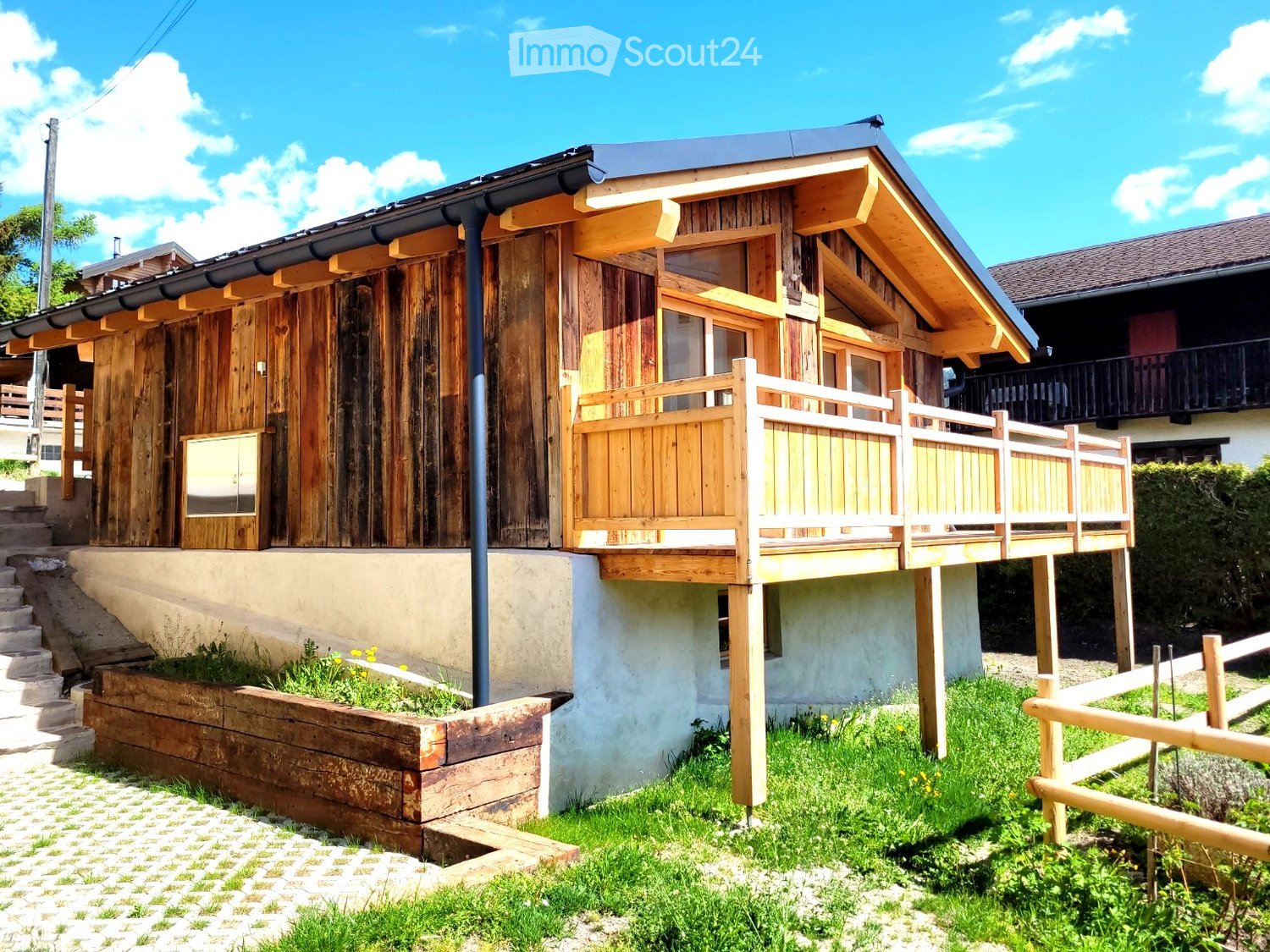 Wooden chalet with a balcony, steps leading up, and a small garden area.