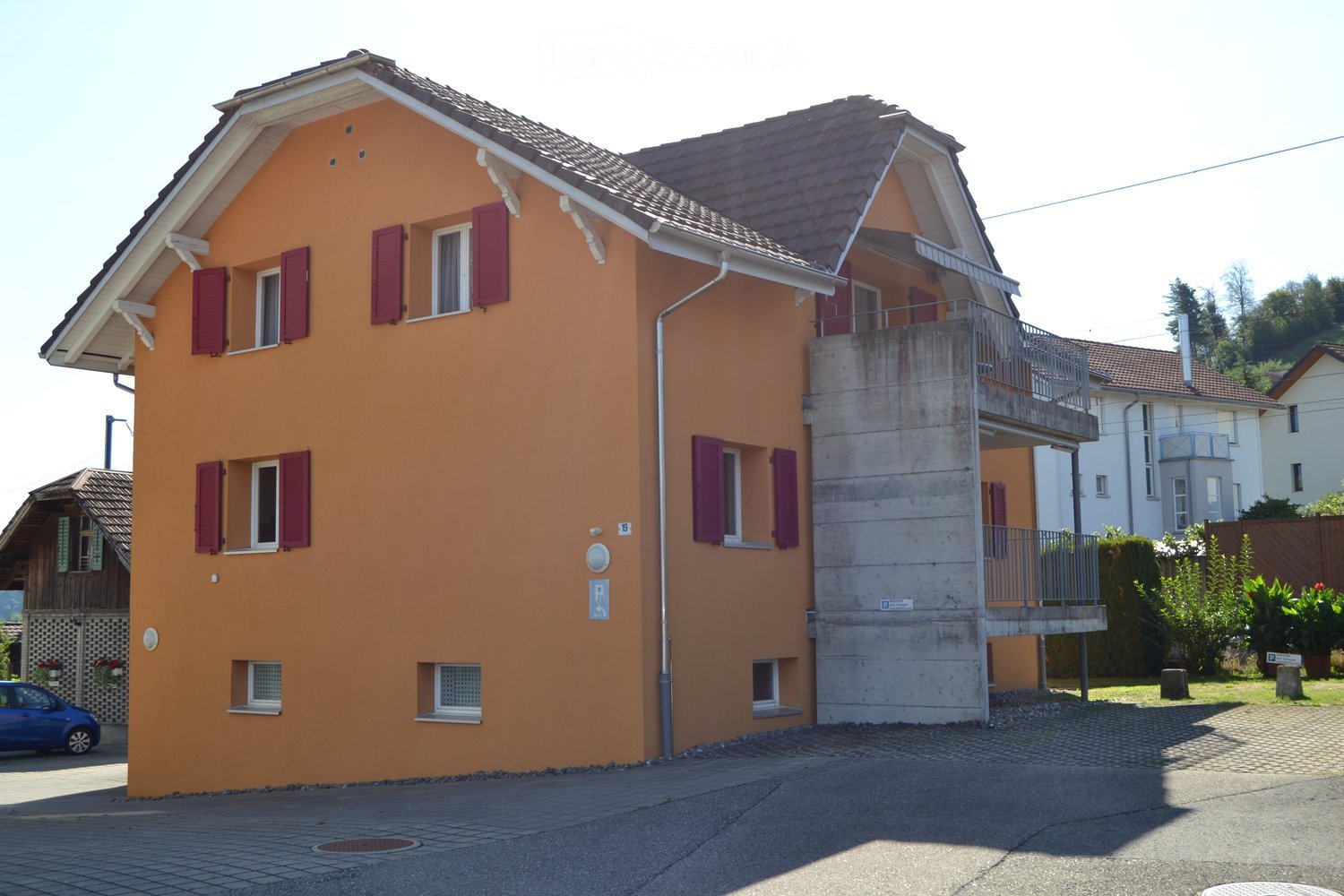 Two-story orange house with red shutters, balcony, and driveway.