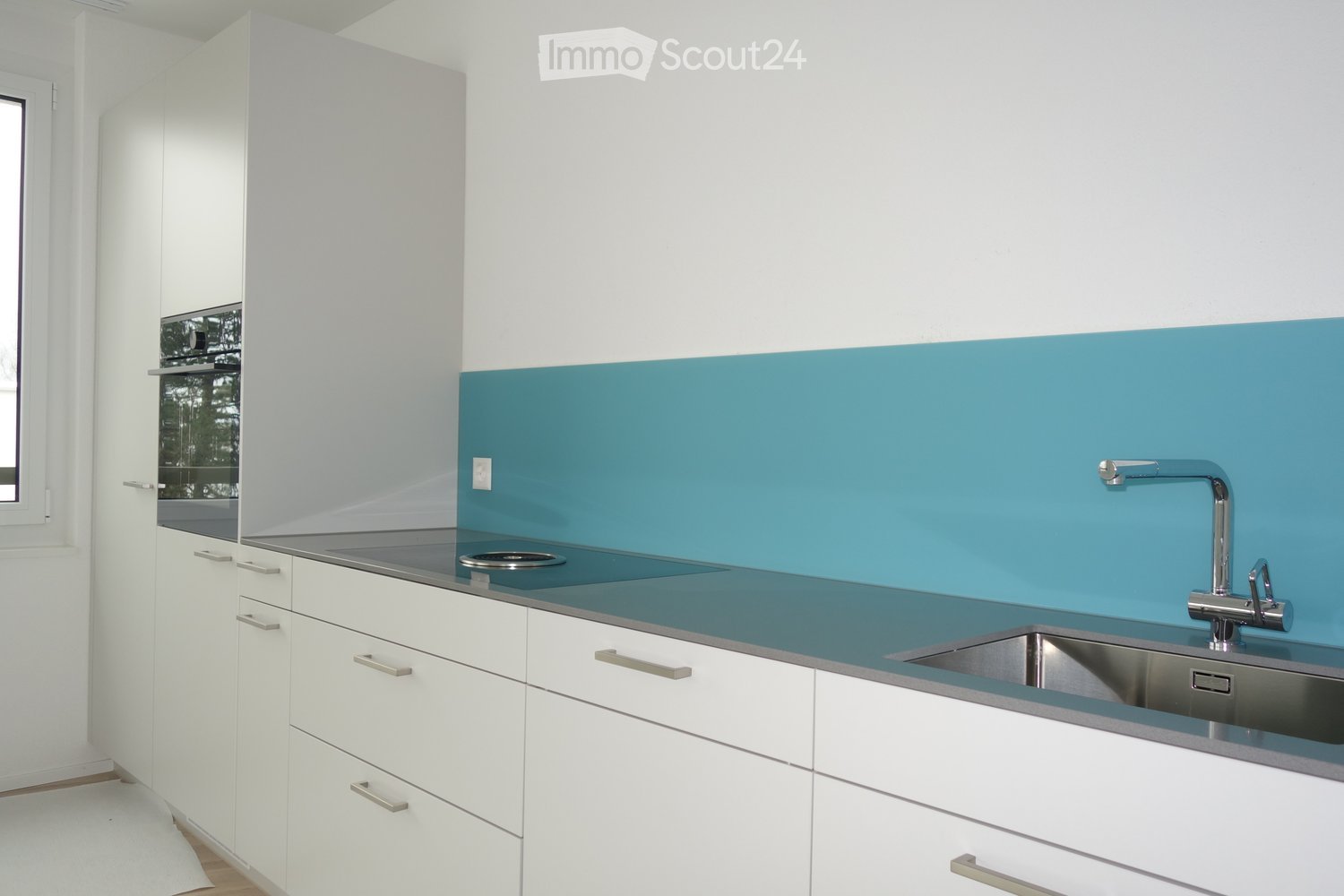 Modern kitchen with white cabinets, stainless steel sink, and a blue accent wall. Features a sleek, minimalist design with a built-in stove and ample storage space.
