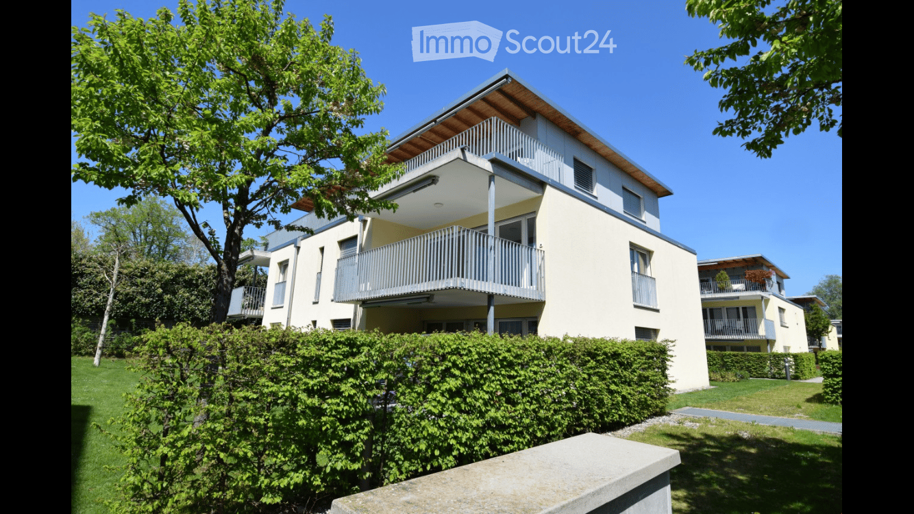Modern two-story residential building with balconies, surrounded by greenery and a well-maintained lawn.
