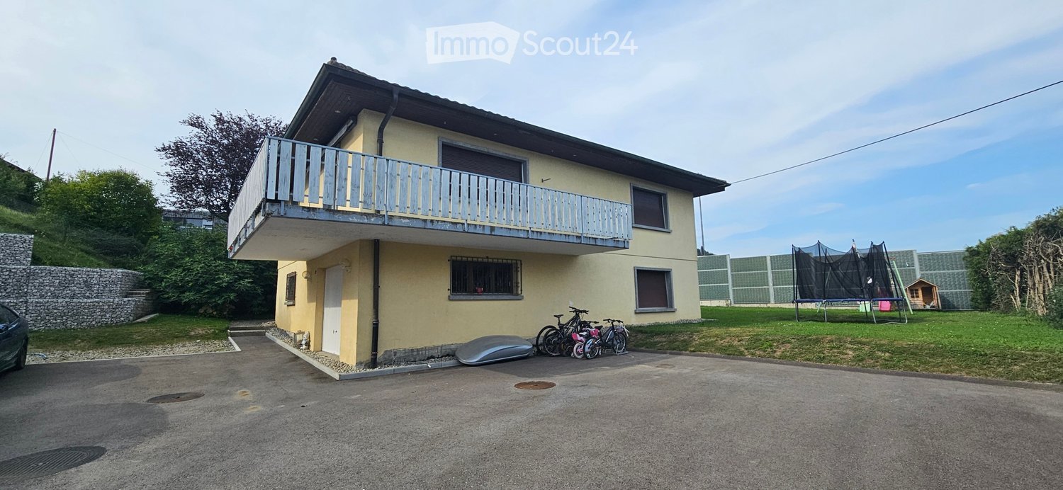Two-story house with a balcony, bicycles, and a trampoline in the yard.