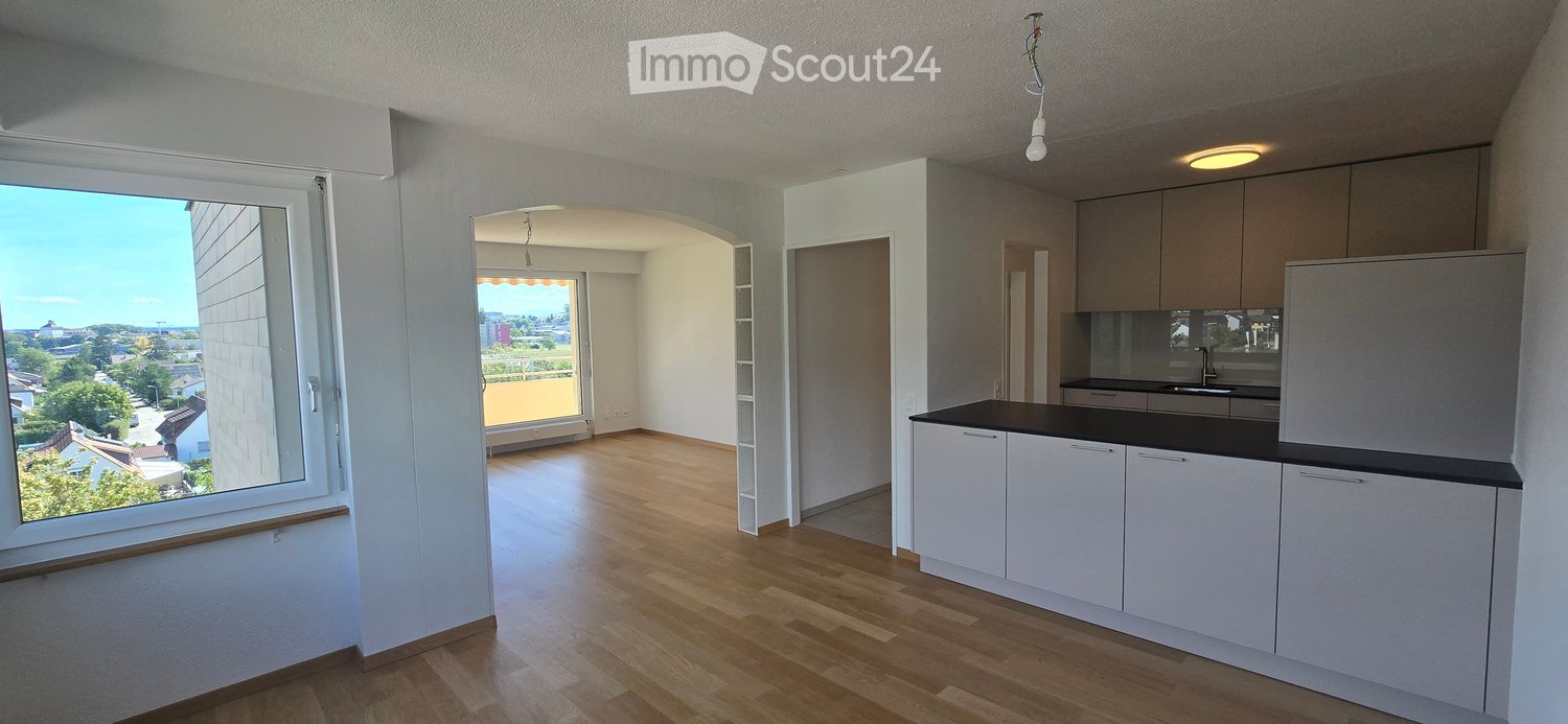 Modern kitchen with white cabinets, black countertop, and a large window offering a view of the city and greenery.