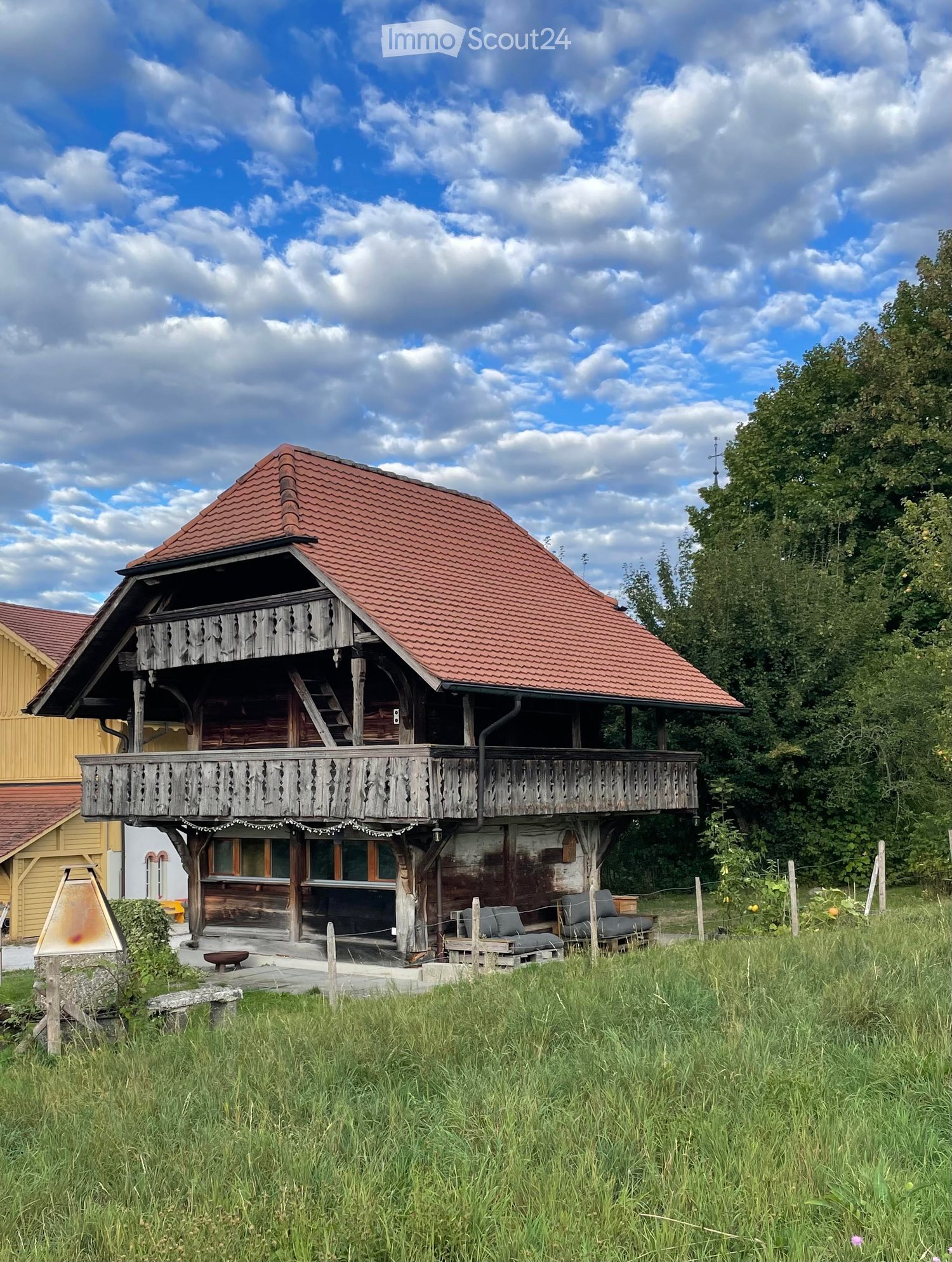 Traditional wooden house with a red-tiled roof, balcony, and outdoor seating area.