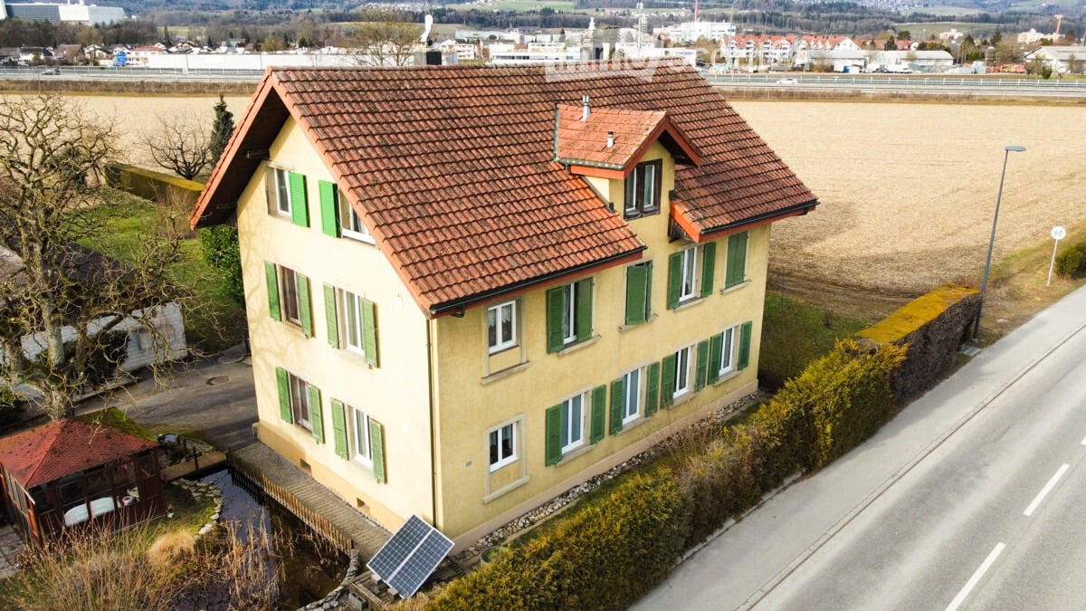 Two-story house with a red-tiled roof, green shutters, and a small pond in the front yard.