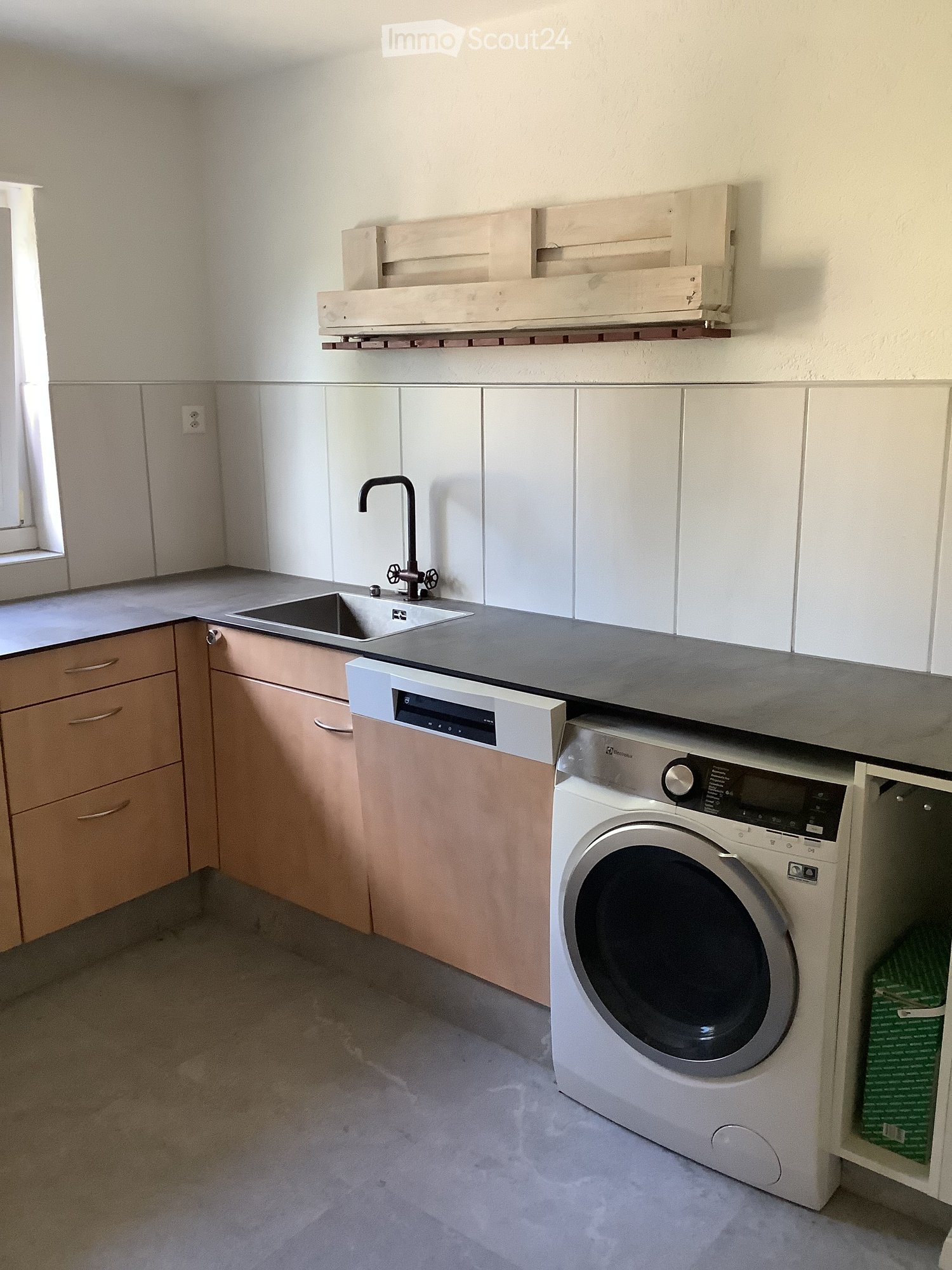 Modern kitchen with light wood cabinets, stainless steel sink and faucet, dishwasher, and washing machine under the counter.