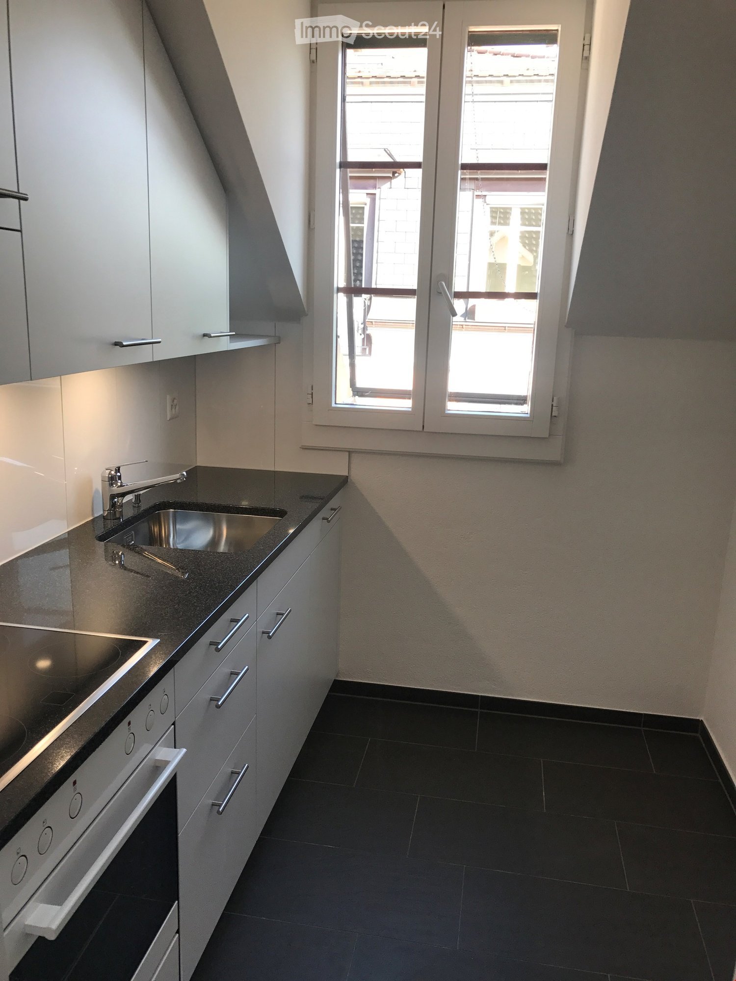 Modern kitchen with white cabinets, black countertops, stainless steel sink, and built-in stove. Features large windows with a view of the outside.