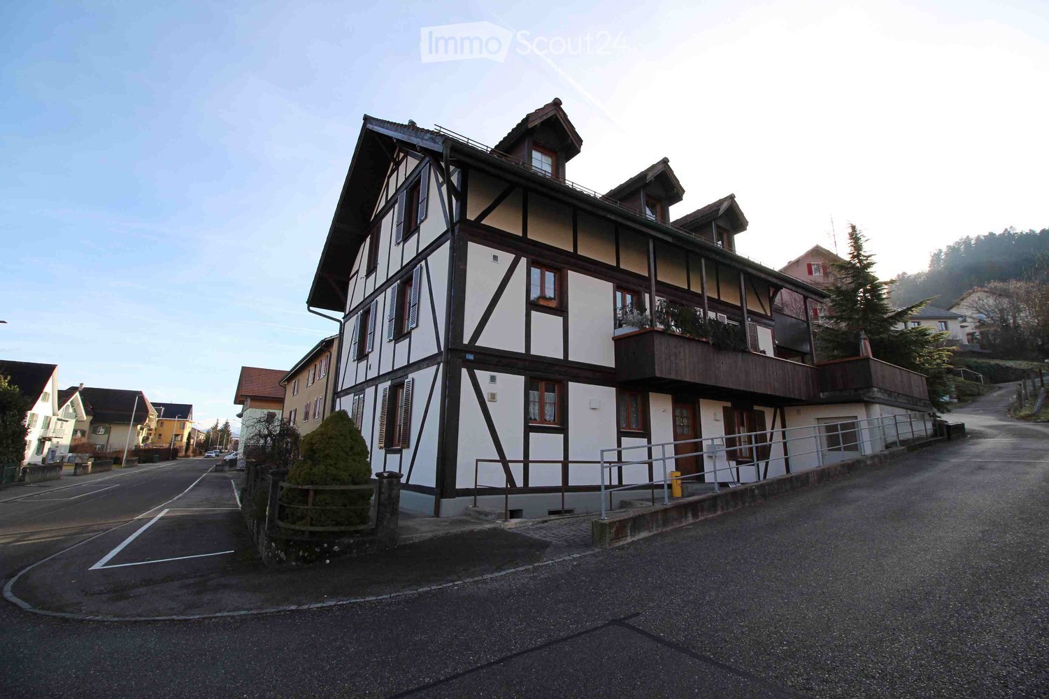 A two-story traditional Swiss house with white and dark wood facade, multiple windows, and a balcony on the upper floor.