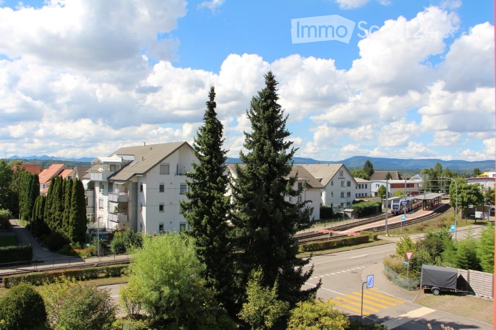 A view of a suburban neighborhood with houses, trees, a train track, and a clear blue sky with scattered clouds.