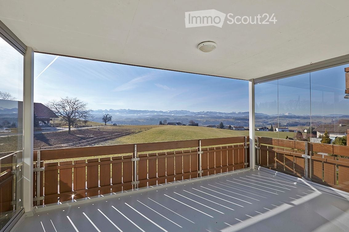 Modern balcony with large glass walls, wooden railing, and scenic mountain view.