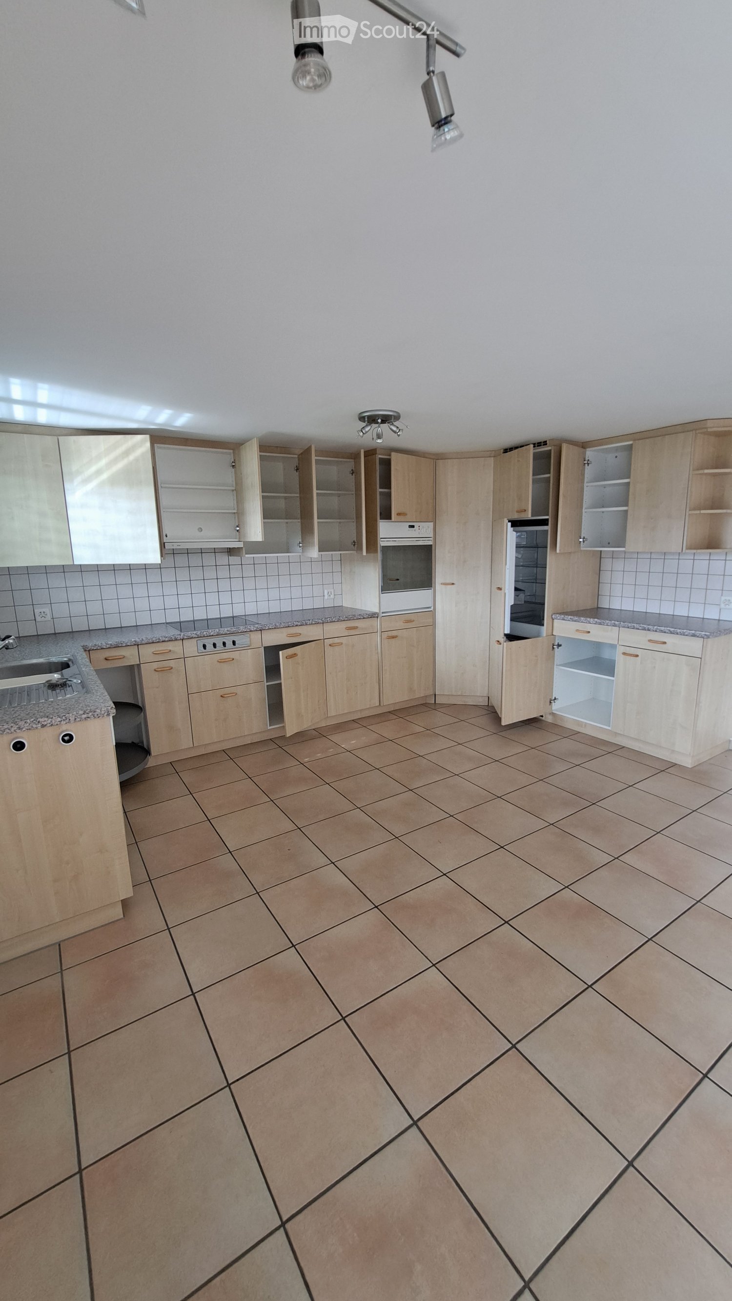 Empty kitchen with light wooden cabinets, granite countertops, and tiled floor. Cabinets are open, revealing empty shelves. No appliances or furniture are present.