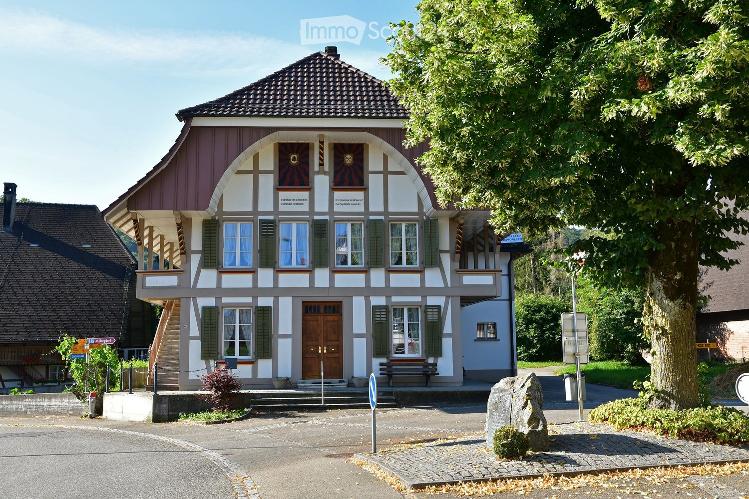 Two-story building with a gabled roof, white and brown exterior, multiple windows with shutters, and a wooden front door.