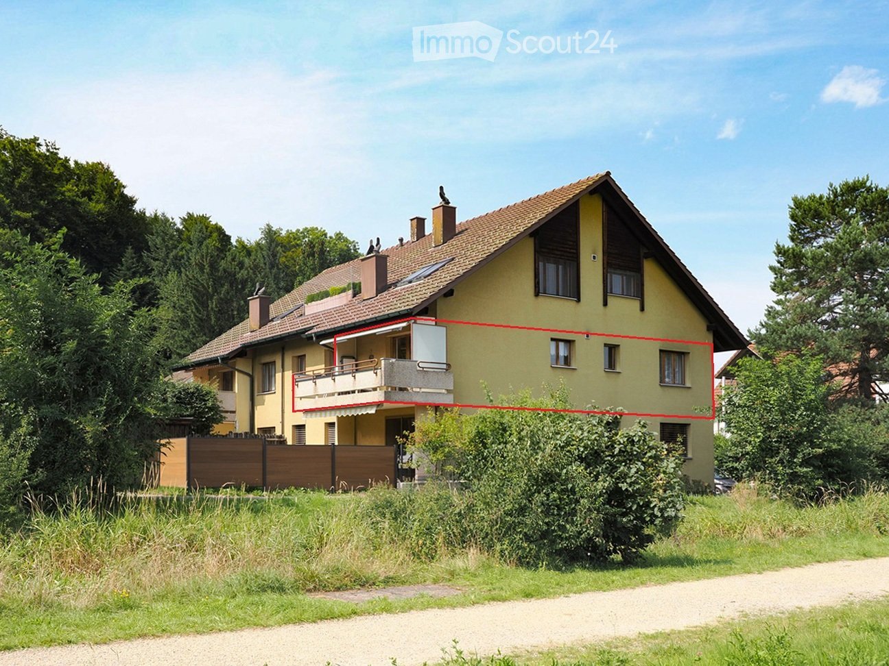 Two-story yellow house with a tiled roof, multiple windows, and a balcony on the upper floor.