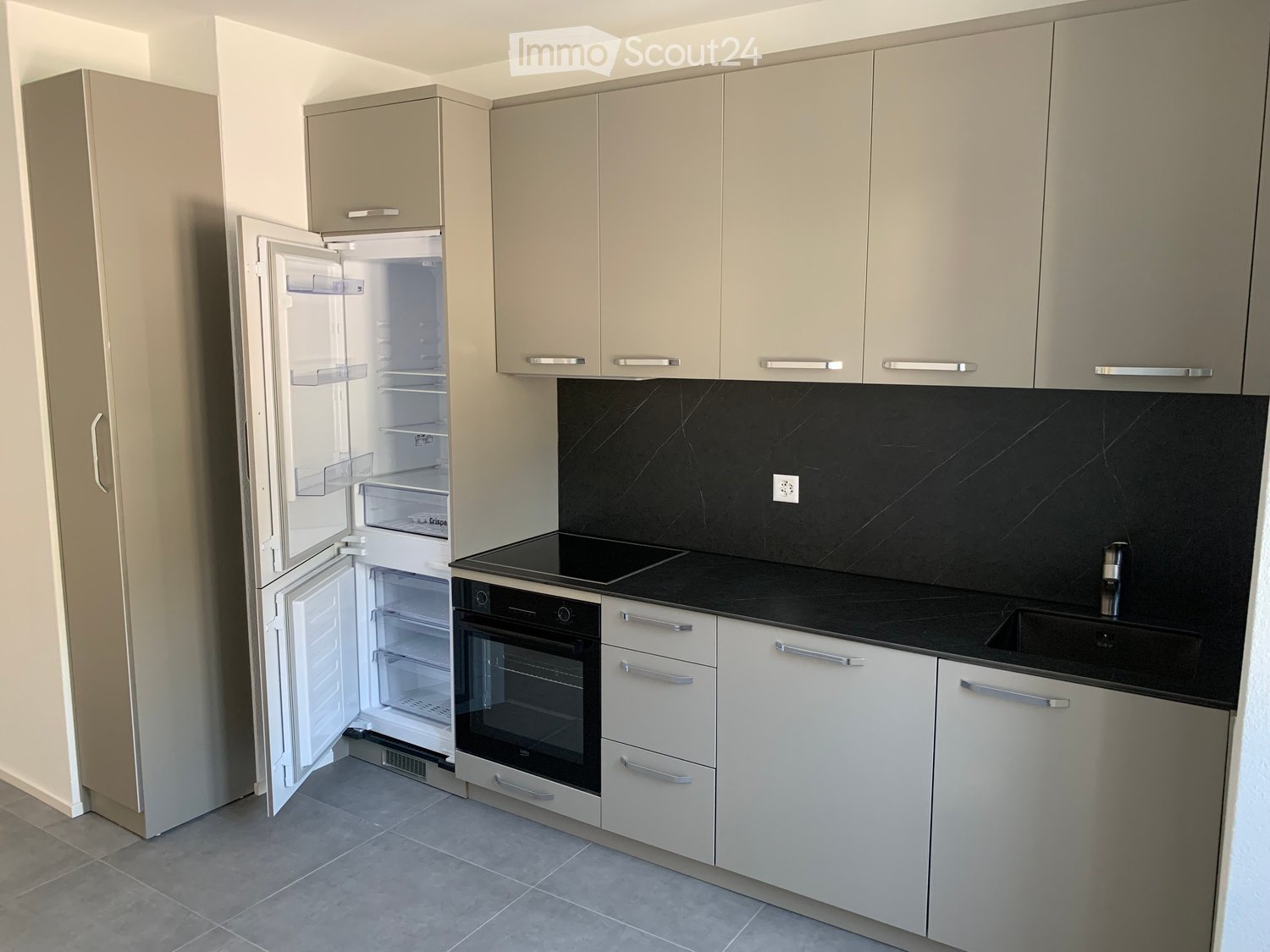 Modern kitchen with light grey cabinets, black countertop, stainless steel appliances, and an open refrigerator.