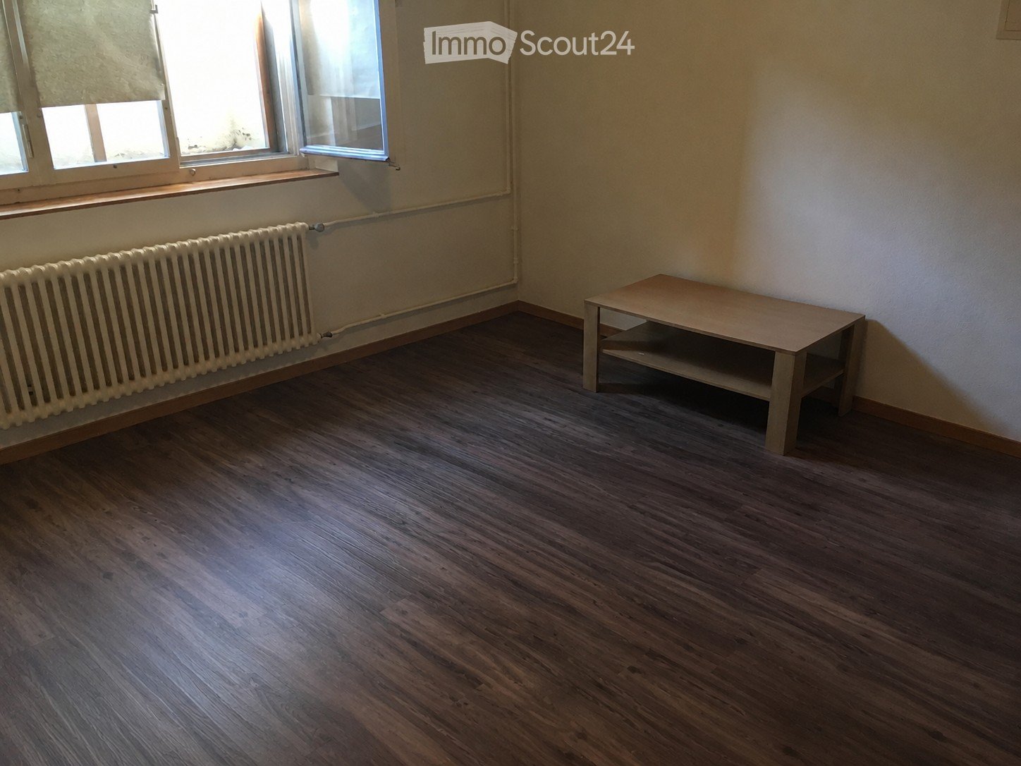 Empty room with wooden flooring, a radiator, and a small wooden table near the window.