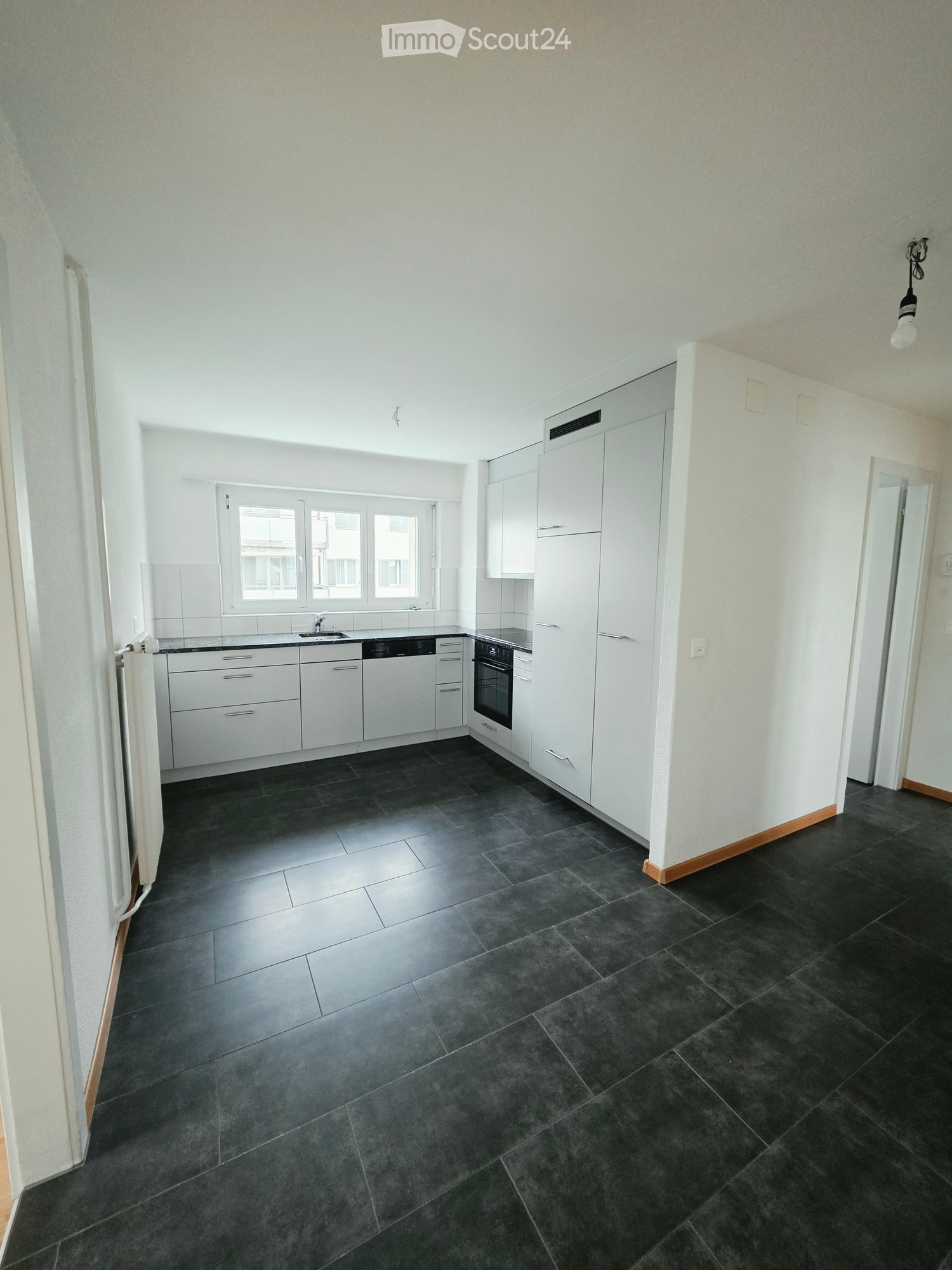 Modern kitchen with white cabinets, dark tiled floor, sink, oven, and dishwasher.
