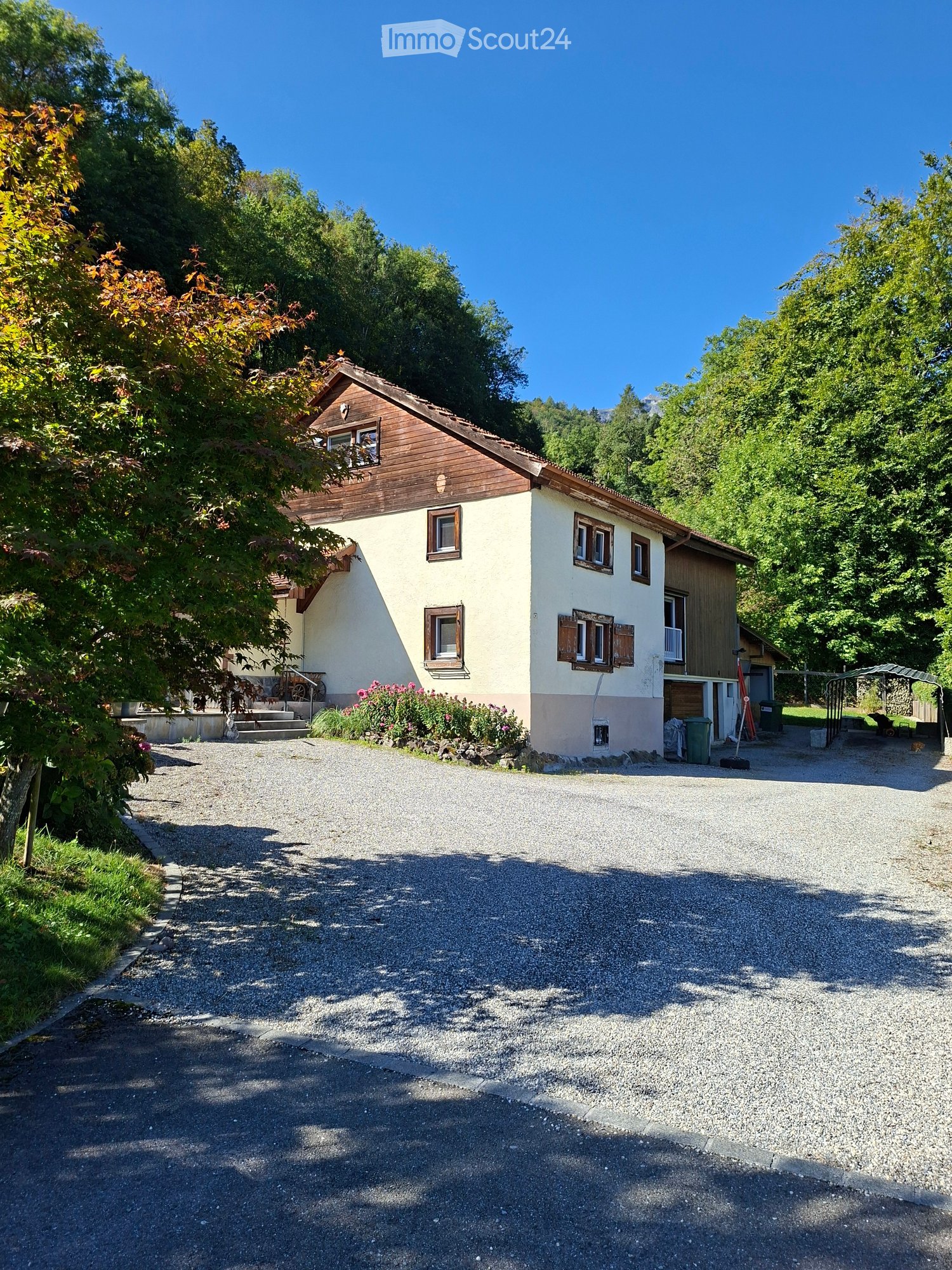 Two-story house with a combination of wood and plaster exterior, multiple windows, and a gravel driveway.
