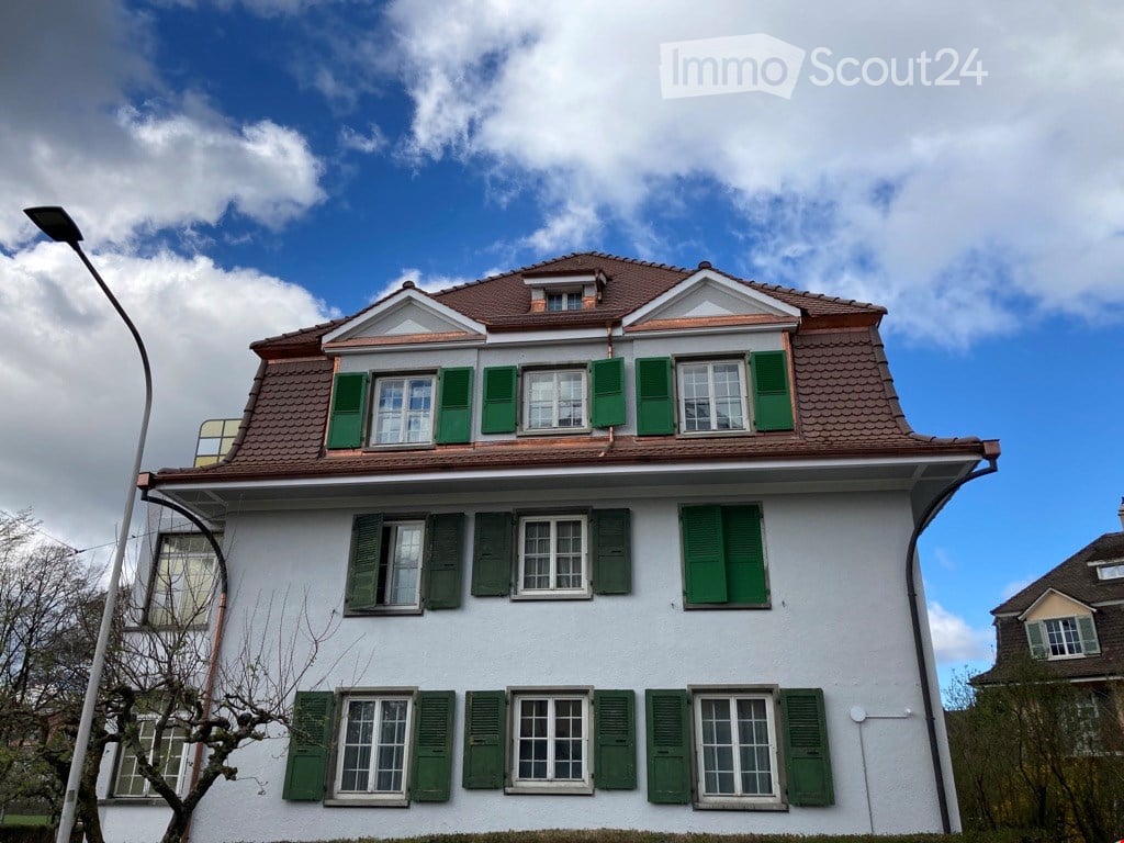 Two-story house with white exterior, green shutters, and a brown tiled roof.