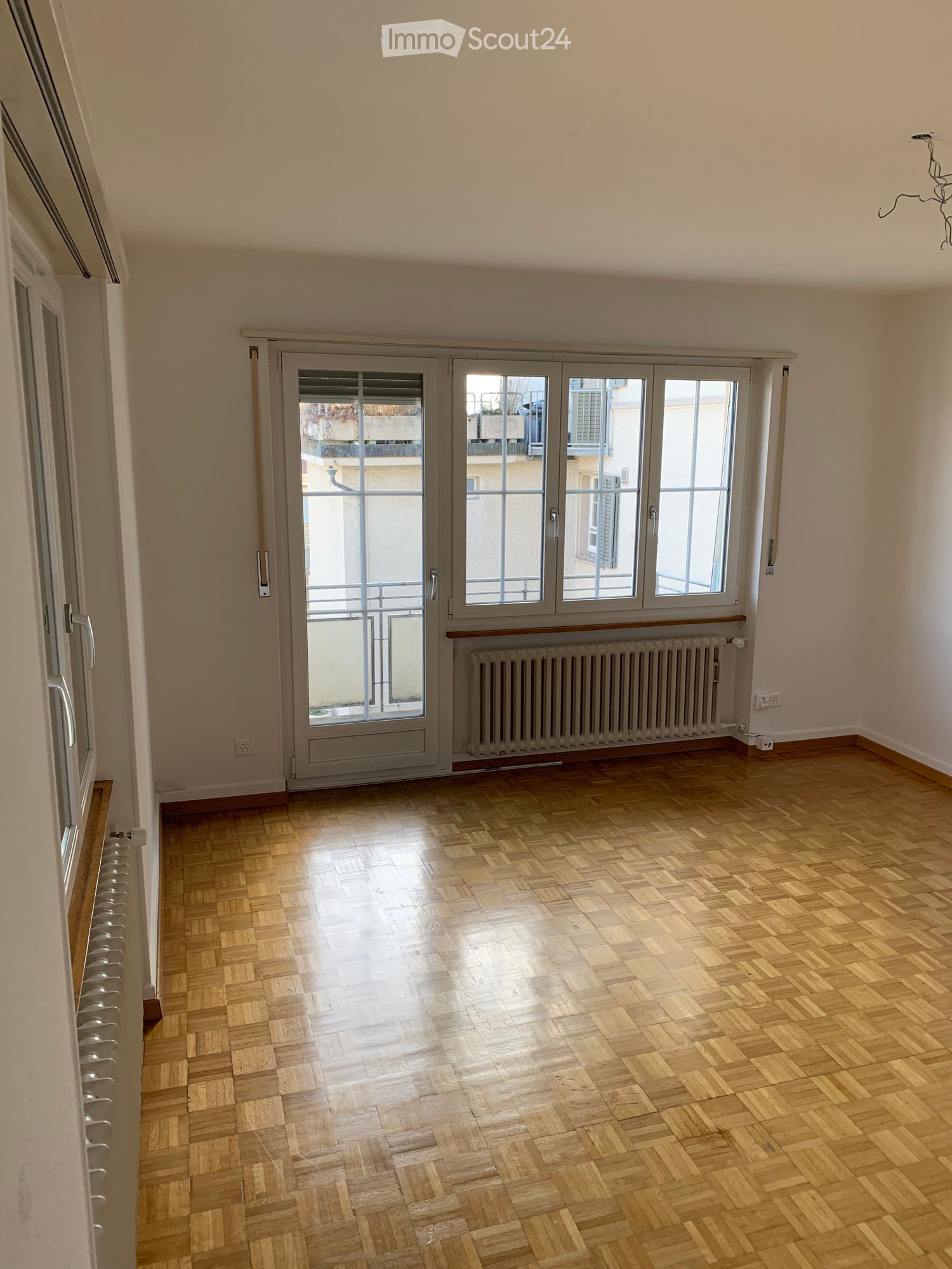 A room with wooden floors, white walls, sliding doors, large windows, heaters, balconies