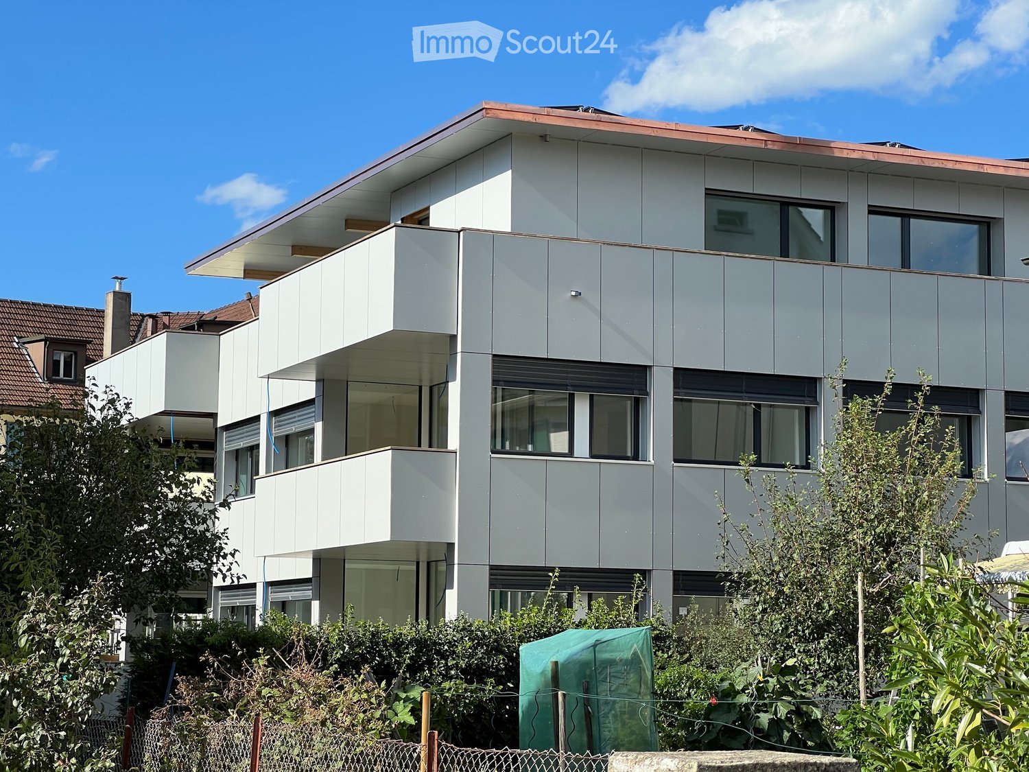 Modern multi-story building with white facade, large windows, and balconies. The structure features a flat roof and contemporary design.