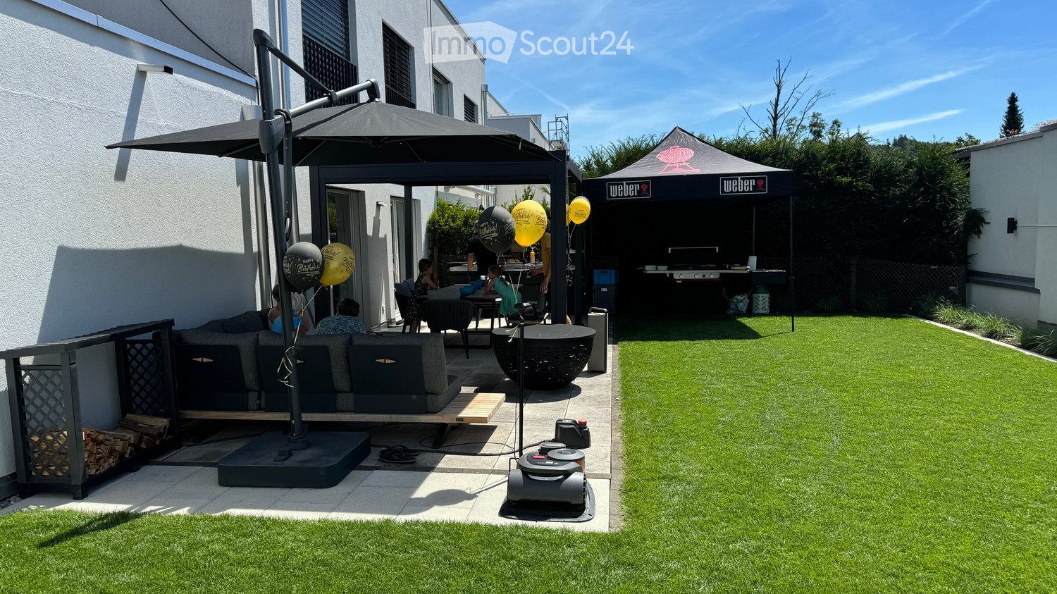 Well-maintained garden with artificial grass, patio seating area, umbrella, Weber grill, and balloons.
