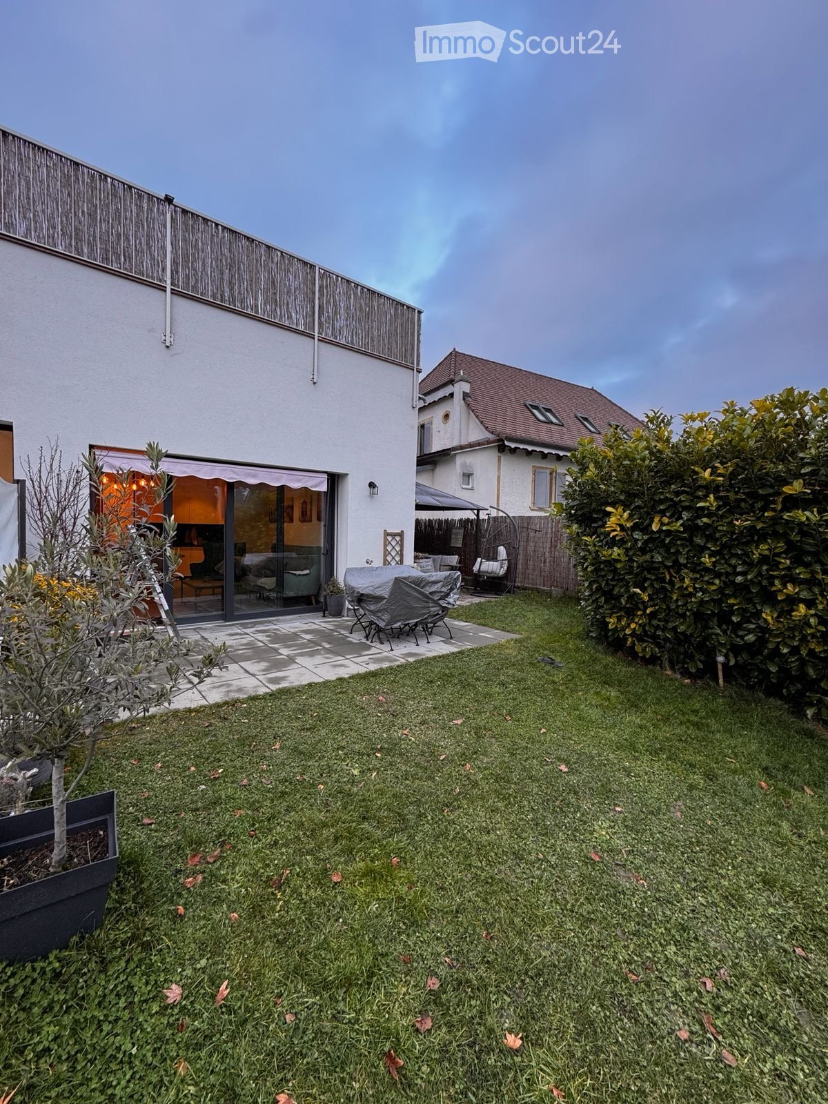 Well-maintained garden with a lawn, patio area, covered seating, and surrounding greenery.