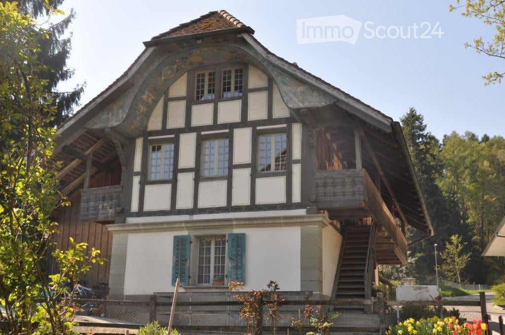 Traditional two-story house with a steep, gabled roof, white and dark wooden facade, multiple windows, and a wooden staircase leading to an upper balcony.