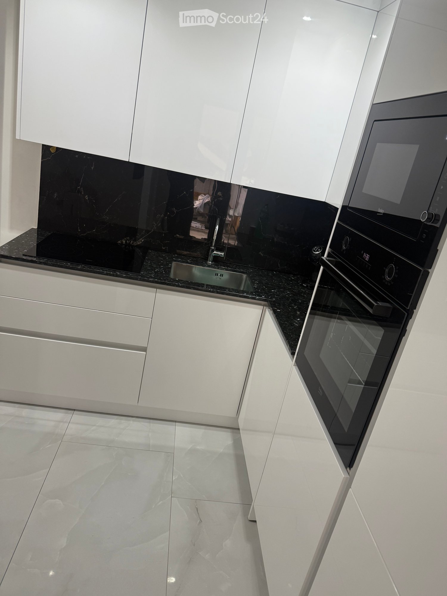 Modern kitchen with white cabinets, black granite countertops, a stainless steel sink, and a built-in oven.