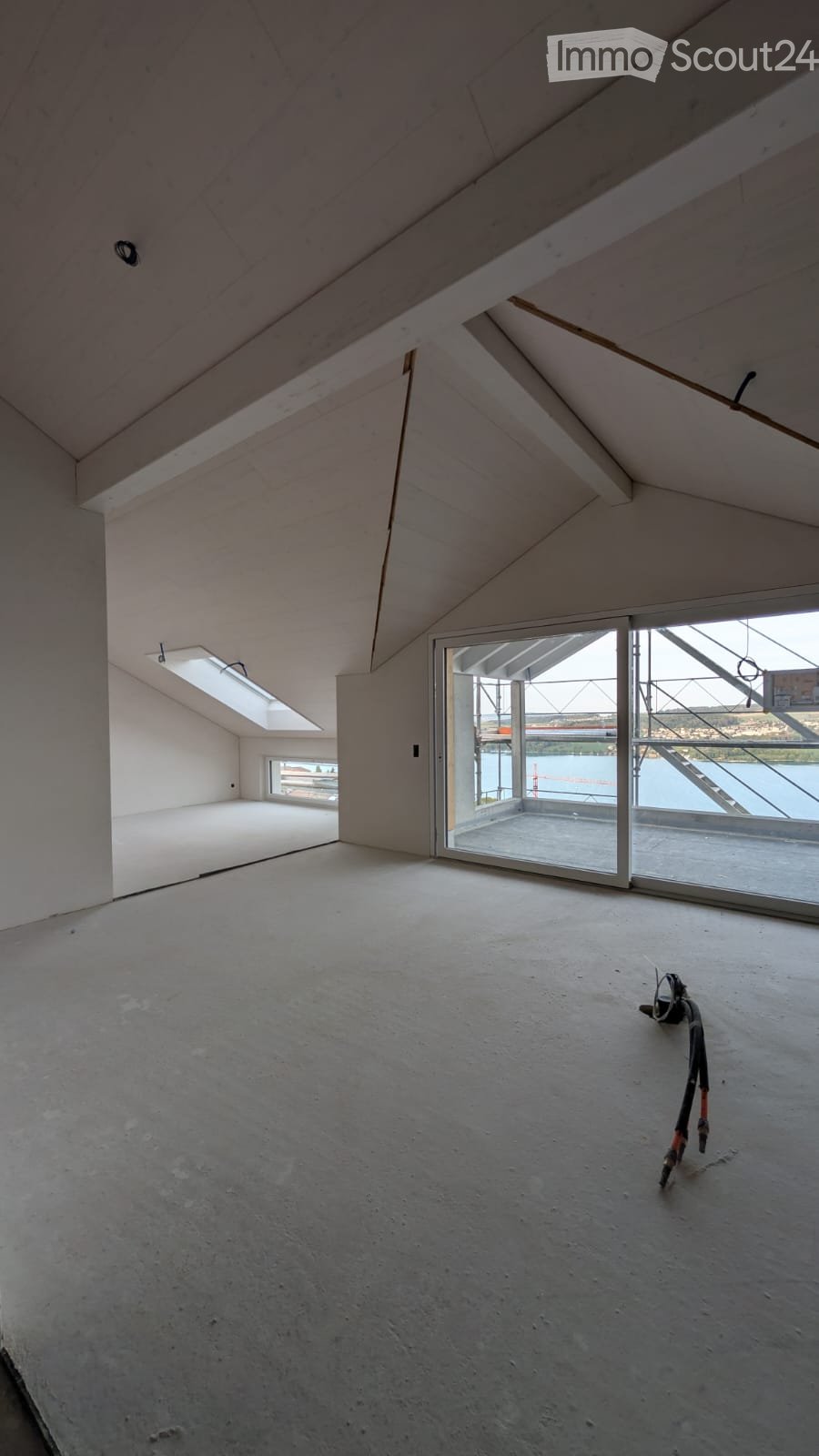 Empty attic space with concrete floor, white walls, skylight windows, and a large glass door leading to a balcony.