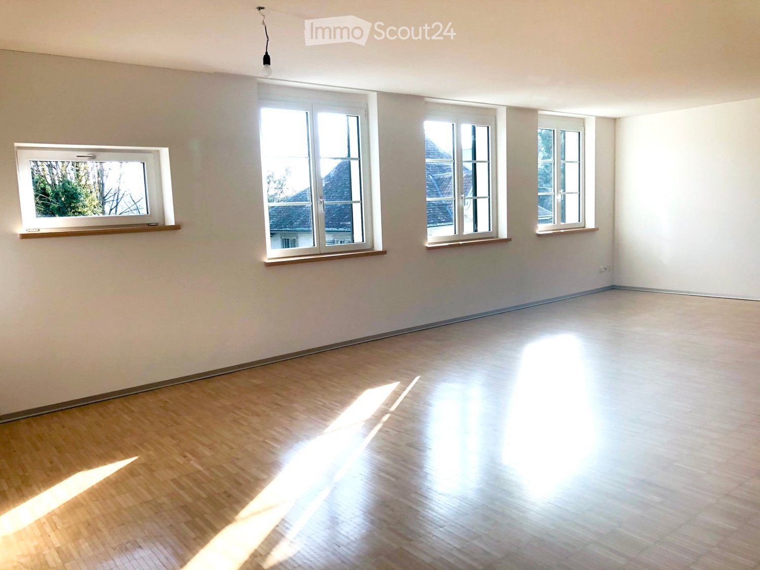 Empty room with wooden flooring and multiple windows allowing natural light to enter.