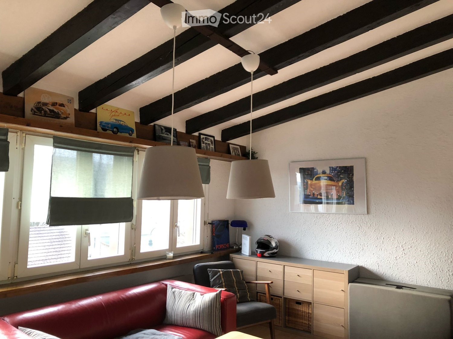 Living room with exposed wooden beams, red leather sofa, armchair, cabinet, and hanging lamps.
