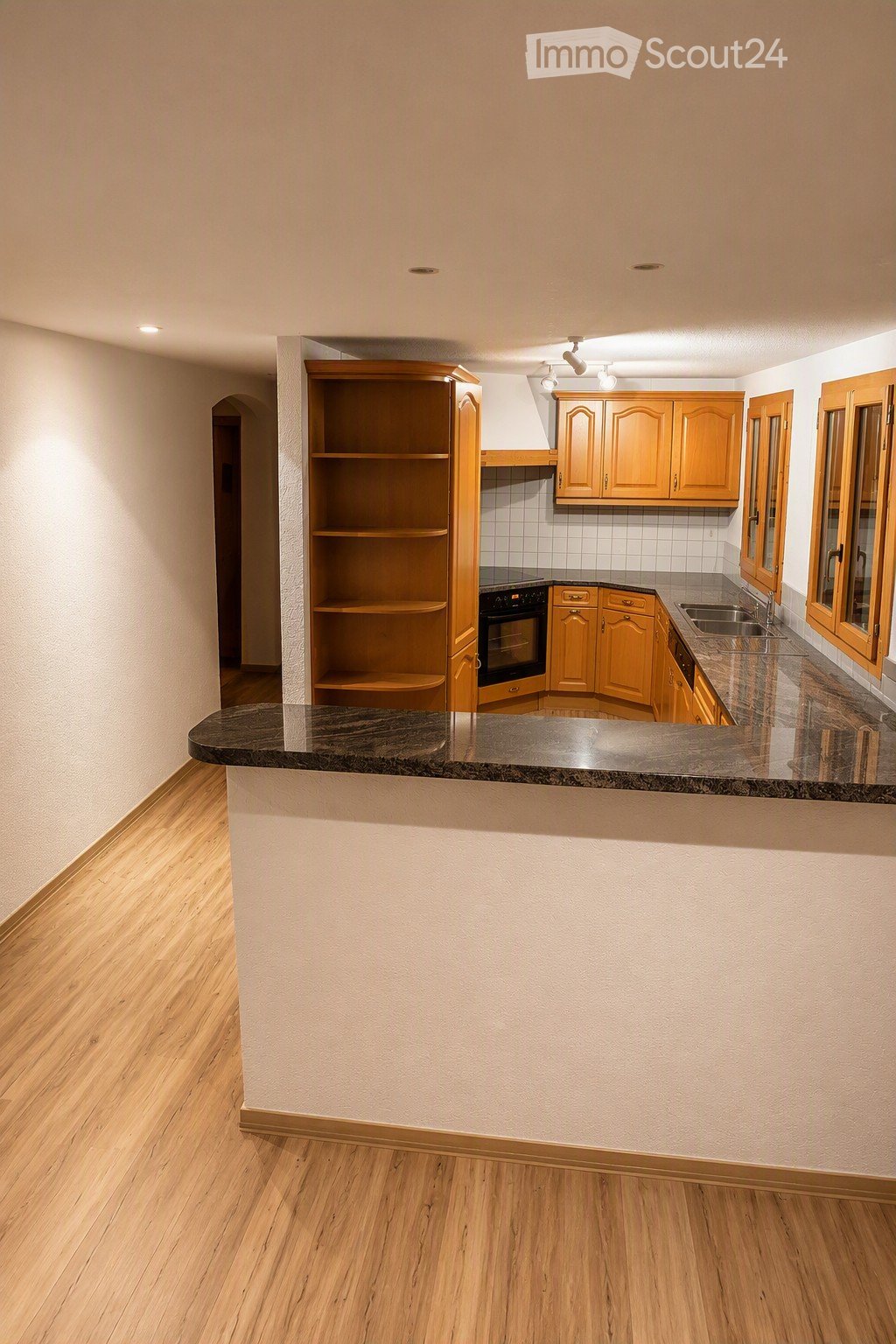 Modern kitchen with wooden cabinets, granite countertop, built-in oven, and sink. Features a wooden floor and large windows.