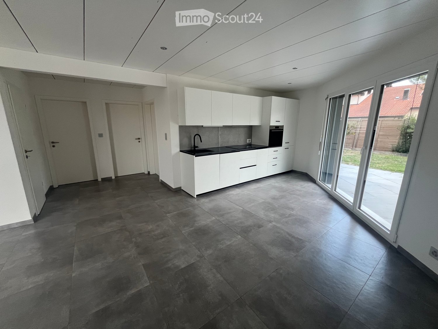 Modern kitchen with white cabinets, dark countertops, and a large window overlooking a garden.