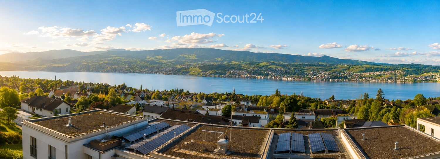 Panoramic view of a town with houses, a lake, and mountains in the background.