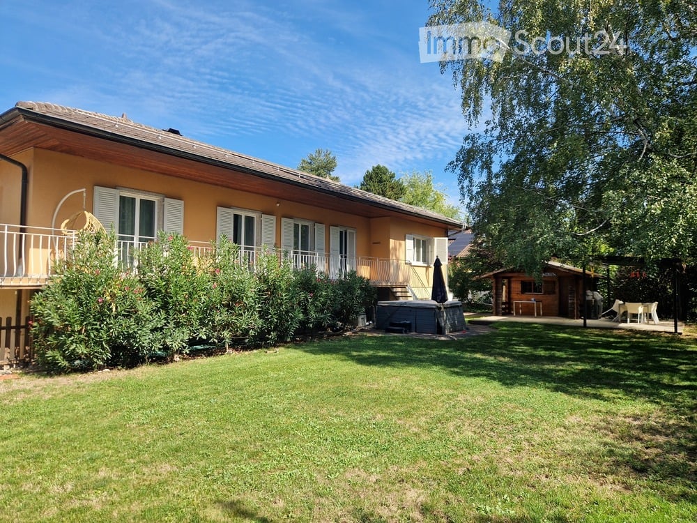 Single-story house with a balcony, surrounded by a well-maintained lawn and a swimming pool.
