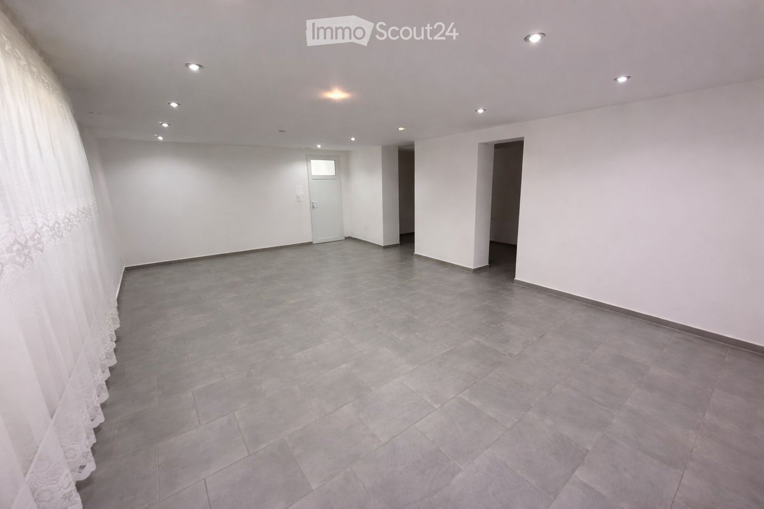 Empty room with white walls, gray tiled floor, a window, and ceiling lights.