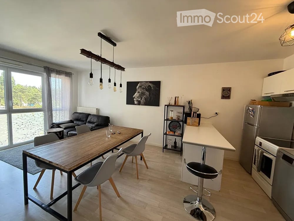 Open-plan living and dining area with a black leather sofa, wooden dining table with chairs, modern kitchen appliances, and pendant lighting.