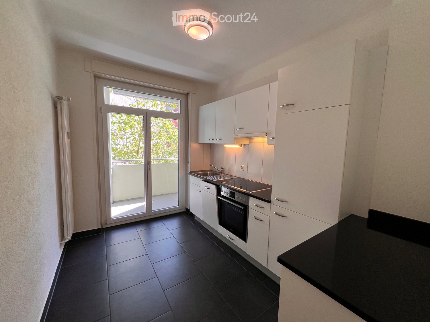 Modern kitchen with white cabinets, black tiled floor, and a black countertop. Features a sink, faucet, and oven.