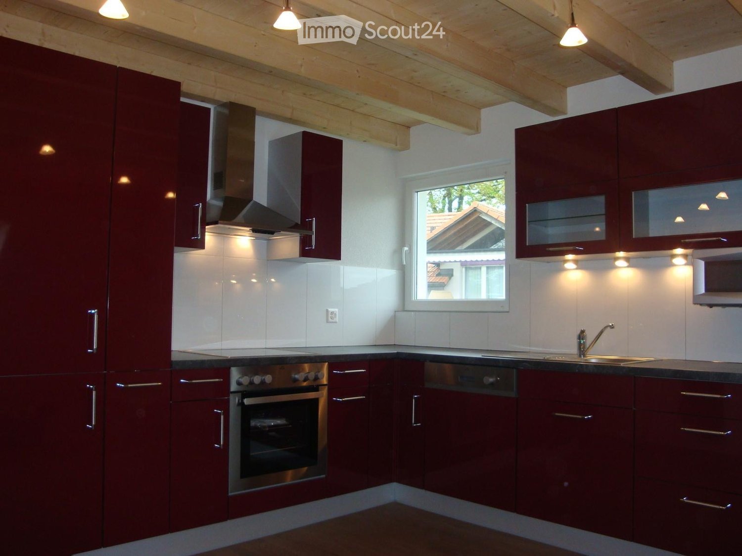 Modern kitchen with dark red cabinets, stainless steel appliances, and a window overlooking a neighboring house.