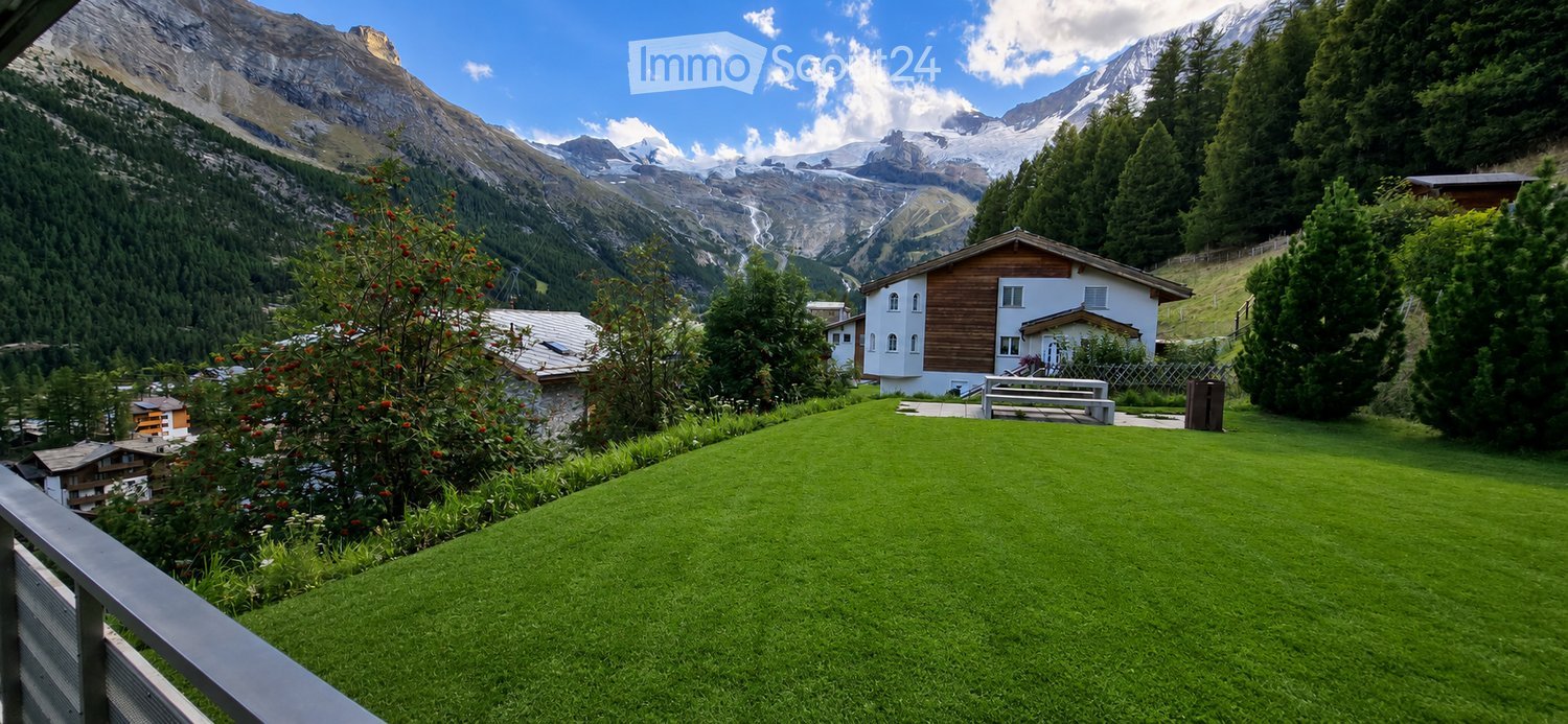 Lush green lawn with a wooden bench, surrounded by trees and mountains in the background.