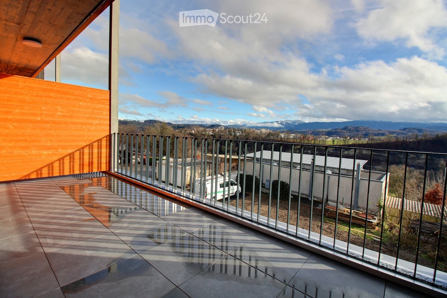 Modern balcony with glass railing, tiled floor, and scenic mountain view.
